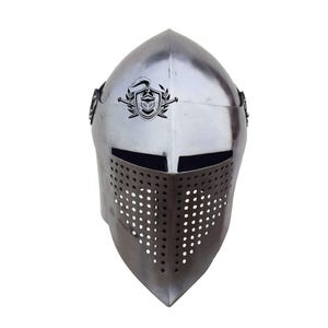 Op de afbeelding: Een zilveren ridderhelm met een vizier met een geperforeerd ontwerp. De helm heeft een kam met een schild en een zwaard.