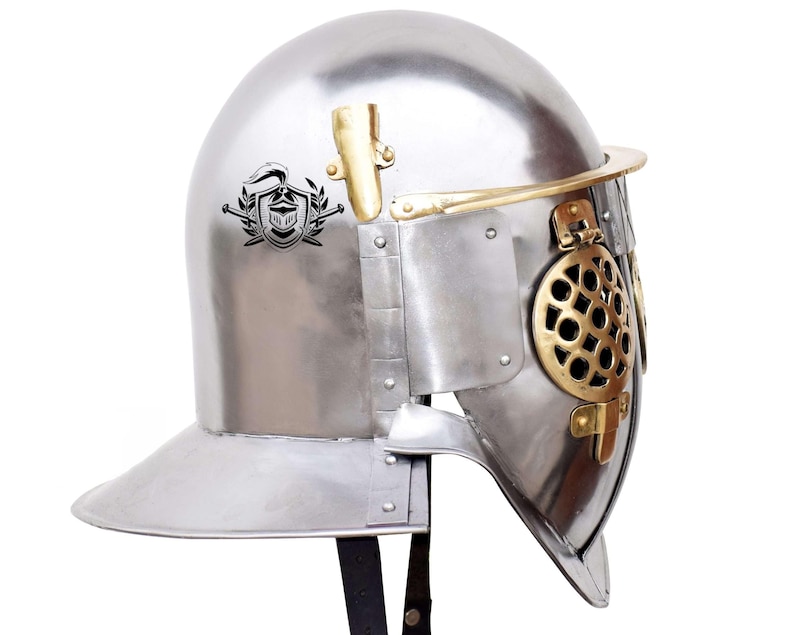 Pode incluir: Um capacete de prata com uma viseira de lat&atilde;o e uma crista decorativa no lado. O capacete tem uma prote&ccedil;&atilde;o de malha para o rosto e uma correia de couro.