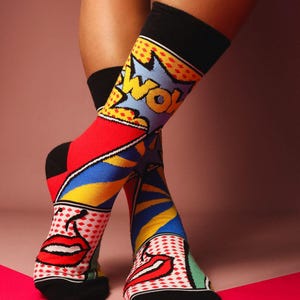 May include: A pair of colourful socks with a pop art design. One sock features a red, yellow and blue design with a speech bubble that says "WOW!" The other sock features a red, yellow, blue and green design with a red lip graphic.