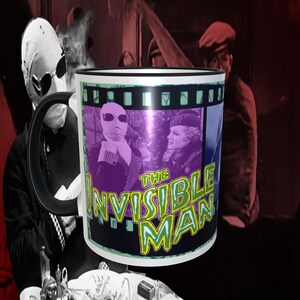 May include: A white ceramic mug with a black rim and handle. The mug features a colorful image of a man in a white bandage over his face, with the text "The Invisible Man" in green and yellow letters.