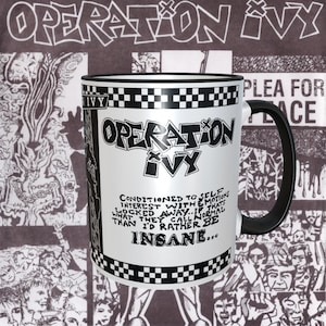 Op de afbeelding: Een witte keramische mok met een zwarte rand en handvat. De mok heeft een zwart-wit geruit patroon rond de rand en een zwart-witte afbeelding van de band Operation Ivy. De afbeelding bevat de bandnaam en de tekst "Conditioned to self interest with emotions locked away: If that's what they call normal than I'd rather be insane..."
