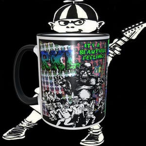 May include: A white ceramic mug with a black handle. The mug features a colourful graphic of a monster with the text "It's a beautiful feeling".