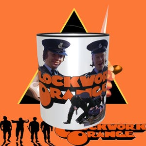 May include: White ceramic mug with a black rim. The mug features a scene from the movie "A Clockwork Orange" with two characters in police uniforms and the film's title in orange letters.