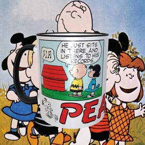 May include: A white ceramic mug with a black handle features a Peanuts cartoon illustration. The mug has a red and white striped design and the text "He just sits in there and listens to his records."  The mug also has the text "PEANUTS" in red letters.