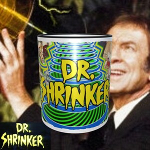 May include: A white ceramic mug with a black rim. The mug features a green and blue swirling pattern with the text "DR. SHRINKER" in yellow letters.