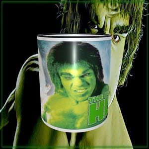 May include: A white ceramic mug featuring a green image of the Hulk with the text "THE IN HULK". The background shows a green Hulk image. The mug has a black rim and handle.