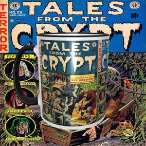 Könnte beinhalten: Eine weiße Keramik-Kaffeetasse mit schwarzem Henkel. Die Tasse zeigt eine Illustration eines Monsters auf einem Vintage-Comic-Cover mit dem Text "Tales from the Crypt" auf der Vorderseite. Das Comic-Cover ist in Schwarz, Weiß, Rot und Blau gehalten.