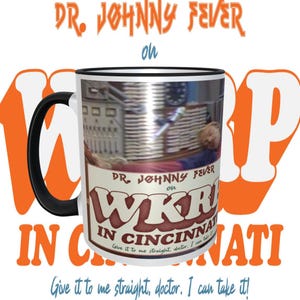 May include: White ceramic coffee mug with a black rim and handle. The mug features a graphic of a radio station logo with the text "DR. JOHNNY FEVER on WKR IN CINCINNATI" and the tagline "Give it to me straight, doctor. I can take it!"