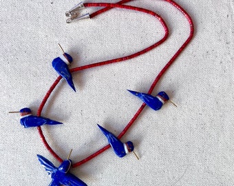 May include: A red coral beaded necklace with five blue hummingbird pendants. The hummingbirds are made of lapis lazuli and have white accents.