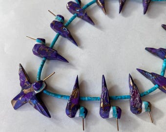 Op de afbeelding: Een streng turquoise kralen met paarse en gouden kolibrie-gravures. De kralen zijn geregen op een draad en klaar om te worden gemaakt tot een ketting of armband.