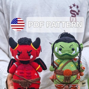 May include: Two crocheted amigurumi dolls: a red devil with horns and a green orc. The devil has black wings and a brown belt. The orc has a brown belt and orange accents. The text "PDF PATTERN" is displayed.