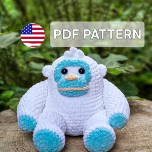 May include: A white and blue crocheted yeti plush toy. The yeti has a light blue face and feet, with black eyes and a tan mouth. The text "PDF PATTERN" is displayed above the yeti. An American flag is in the upper left corner.