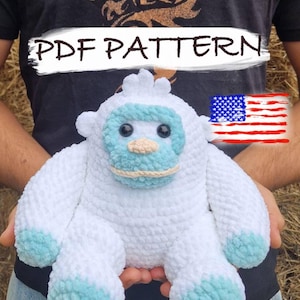 May include: A white and light blue crochet yeti plush toy. The yeti has a light blue face and feet, with black eyes and a beige mouth. The text "PDF PATTERN" is written across the top of the image. An American flag is also visible.
