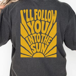 Może przedstawiać: Ciemnoszara koszulka z ż&oacute;łtą grafiką na plecach z napisem "I'll Follow You Into The Sun". Grafika jest w stylu retro i przedstawia słońce. Słowo "Pepper" jest wydrukowane na dole.