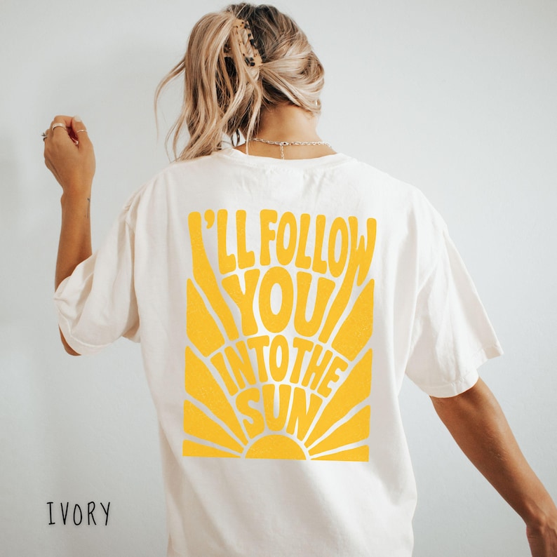 Może przedstawiać: Kremowa koszulka z ż&oacute;łtą grafiką na plecach. Grafika głosi "I'll Follow You Into The Sun" w stylu retro, z motywem promieni słonecznych. Koszulka ma luźny kr&oacute;j.