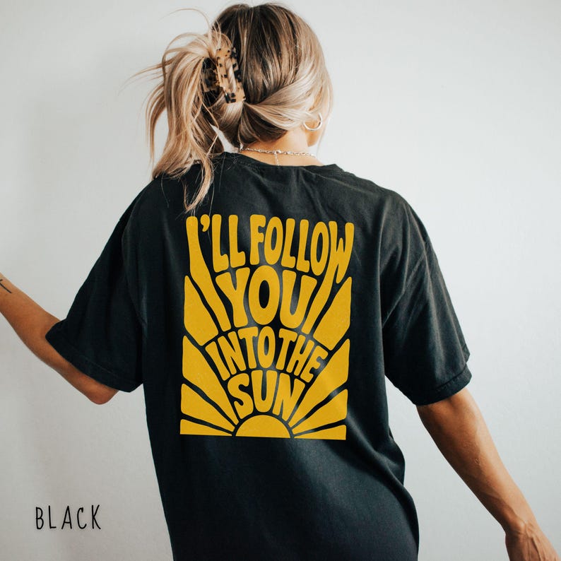 Może przedstawiać: Czarny t-shirt z ż&oacute;łtą grafiką słońca i napisem "I'll Follow You Into The Sun". Koszulka ma luźny kr&oacute;j i kr&oacute;tkie rękawy. Słowo "BLACK" jest wydrukowane na dole koszulki.