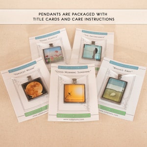 May include: Five glass tile photo pendants with different nature scenes. Each pendant is packaged with a white card with the title of the image and the website address "www.ndtphoto.com". The titles are "Harvest Moon", "Rising Poppies", "The Daydreamer", "Good Morning Sunshine", and "Washed Away".