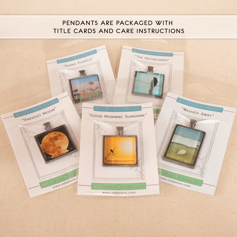 May include: Five glass tile photo pendants with different nature scenes. Each pendant is packaged with a white card with the title of the image and the website address "www.ndtphoto.com". The titles are "Harvest Moon", "Rising Poppies", "The Daydreamer", "Good Morning Sunshine", and "Washed Away".