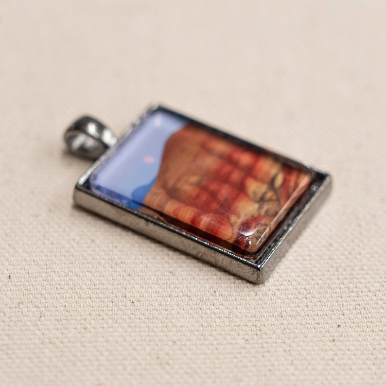 May include: A silver pendant with a rectangular glass insert featuring a colorful abstract design. The design includes shades of red, orange, yellow, blue, and white.