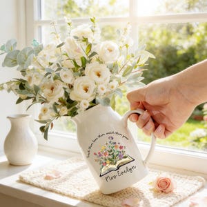 May include: A white ceramic mug with a black handle and the text "But First, Coffee" in a bold, black font. The mug is set against a blurred background, suggesting a cozy setting.