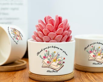 May include: White ceramic planter with a floral design and the text "Thank you for helping me grow" and "Miss Green". The planter has a wooden base and is filled with a pink succulent.