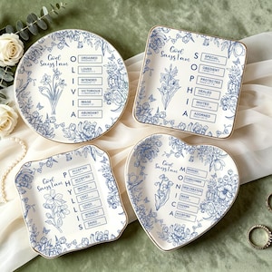 May include: Four decorative plates with floral designs and gold rims. Each plate has a different shape: round, square, heart, and a square with curved edges. The plates feature blue floral patterns and text that reads "God Says I Am."