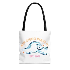 Könnte beinhalten: Weiße Tragetasche mit schwarzen Henkeln. Sie zeigt ein blaues und orangefarbenes Wellenmuster, den Text "SAN DIEGO WAVE FC" und "EST. 2021". Die Tasche besteht aus einem strapazierfähigen Material und eignet sich zum Tragen verschiedener Gegenstände.