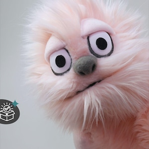 Könnte beinhalten: Eine rosa Plüschpuppe mit großen, ausdrucksstarken Augen und einer grauen Nase. Die Puppe hat ein flauschiges, strukturiertes Aussehen und einen leicht traurigen Ausdruck. Der Text "Finished Item - Ready to Ship" ist zu sehen.