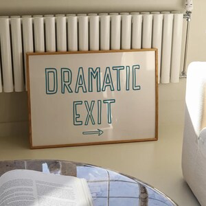 May include: A framed print with a white background and a teal blue outline of the text "Dramatic Exit" with an arrow pointing to the right.