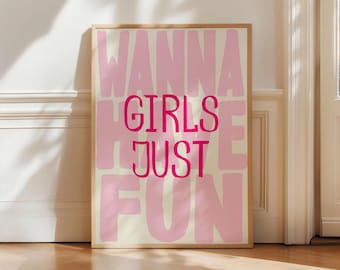 May include: A framed art print with the words "WANNA GIRLS JUST FUN" in pink lettering. The words are stacked in a playful arrangement against a cream-colored background. The frame is a light brown color.