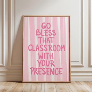 May include: A framed print with a pink and white striped background. The text "GO BLESS THAT CLASSROOM WITH YOUR PRESENCE" is written in pink. The frame is a light brown color.