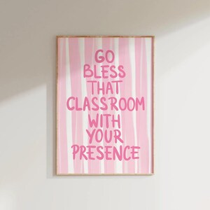 May include: A framed print with a pink and white striped background. The text "GO BLESS THAT CLASSROOM WITH YOUR PRESENCE" is written in pink, bold letters. The artwork is in a wooden frame.