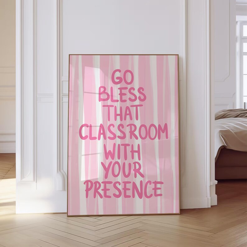 May include: A framed art print with the text "GO BLESS THAT CLASSROOM WITH YOUR PRESENCE" in pink lettering. The background features vertical stripes of pink and white. The frame is a light brown color.