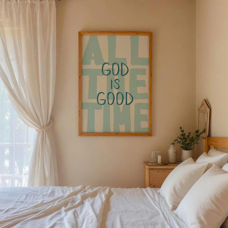 May include: A framed wall art print with the words "ALL GOD IS GOOD TIME" in light blue on a white background. The frame is made of light brown wood. The art hangs above a bed with white bedding.