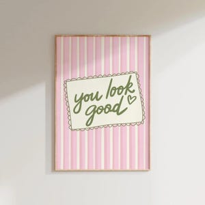 May include: A framed print with a pink and white striped background. The print features a white rectangle with a scalloped edge, containing the words "you look good" in green script, with a small heart symbol.