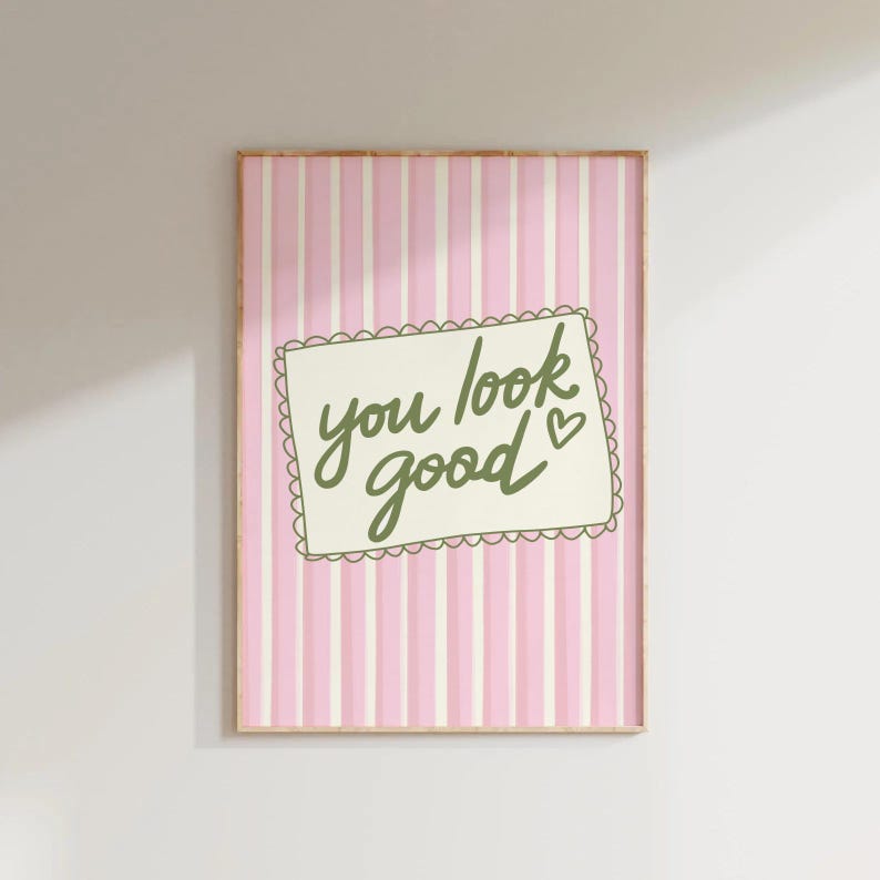 May include: A framed print with a pink and white striped background. The print features a white rectangle with a scalloped edge, containing the words "you look good" in green script, with a small heart symbol.