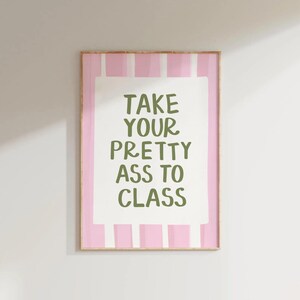 May include: A framed print with a pink and white striped background. The print features the text "TAKE YOUR PRETTY ASS TO CLASS" in green letters on a white rectangular background. The frame is a light brown color.