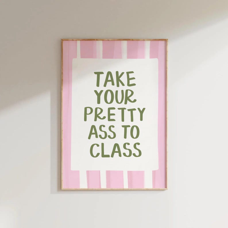 May include: A framed print with a pink and white striped background. The print features the text "TAKE YOUR PRETTY ASS TO CLASS" in green letters on a white rectangular background. The frame is a light brown color.