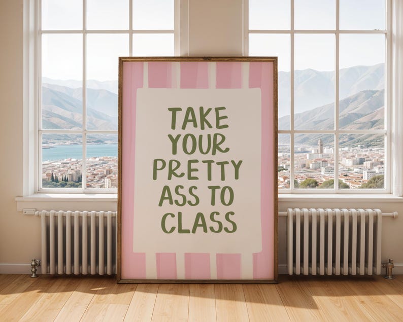 May include: A framed art print with the text "TAKE YOUR PRETTY ASS TO CLASS" in green lettering. The print has a pink and white striped border and is displayed in a room with a window overlooking a city and mountains.