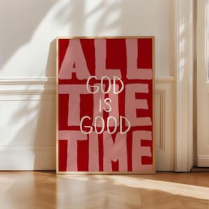 Peut inclure: Une affiche encadrée avec les mots "ALL GOD IS GOOD TIME" dans une police de caractères audacieuse et en blocs. Le fond est rouge foncé, avec les mots en rose clair et blanc. L'œuvre est exposée sur un sol en bois.
