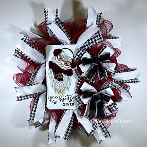 May include: A red and white wreath with black and white houndstooth ribbon. A white sign with a cartoon owl wearing glasses and a red scarf says "Zero Hoots Given".