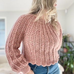 以下が含まれることがあります： フリルのある裾と長袖のピンクのクロシェ編みセーター。セーターはテクスチャのあるステッチで編まれており、ゆったりとしたフィット感です。