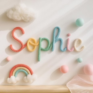Può includere: Decorazione murale con il nome "Sophie" in lettere di filo di lana multicolore. Le lettere sono nei toni del rosso, giallo, verde, blu e rosa. Sono presenti anche un arcobaleno e delle nuvole.