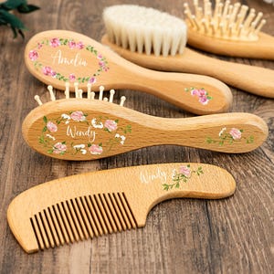 Può includere: Spazzole e pettini per capelli per bambini in legno con disegni floreali e nomi personalizzati. Le spazzole hanno setole morbide e i pettini denti fini. I nomi "Amelia" e "Wendy" sono visibili sulle spazzole.