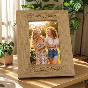 May include: A rectangular light brown wooden picture frame with a textured grain finish. The top of the frame is engraved with the text Forever Friends and the bottom is engraved with the names Sophia & Amelia. The frame holds a photograph of two people.