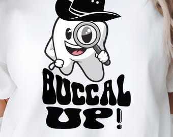 Op de afbeelding: Wit T-shirt met een cartoon tand die een detective hoed draagt en een vergrootglas vasthoudt. De tekst "BUCCAL UP!" staat eronder in een retro lettertype. Een casual kledingstuk voor dagelijks gebruik.