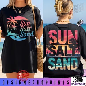 May include: Black t-shirt with a colorful graphic design. The front features the words "Sun Salt Sand" with a sunset and palm tree design. The back of the shirt also displays the words "Sun Salt Sand" in a similar style. The shirt is a casual wear item.