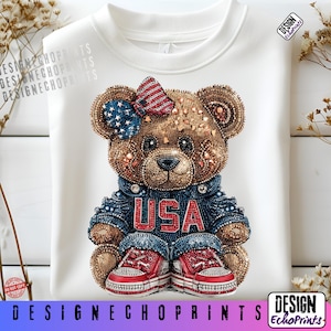 Puede incluir: Una sudadera blanca con una ilustraci&oacute;n detallada de un oso de peluche. El oso est&aacute; adornado con elementos patri&oacute;ticos, incluyendo un lazo con un dise&ntilde;o de estrellas y rayas, una chaqueta vaquera con la inscripci&oacute;n "USA" y zapatillas rojas. El dise&ntilde;o incorpora pedrer&iacute;a.