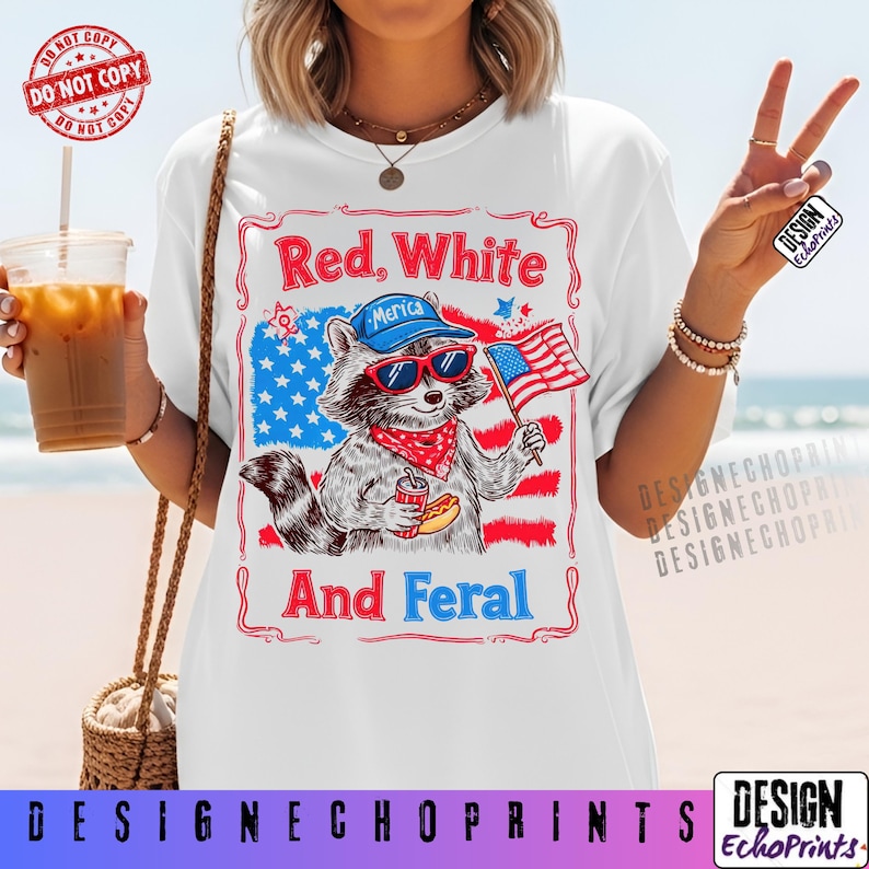 Puede incluir: Camiseta blanca con un dise&ntilde;o de mapache con gafas de sol, pa&ntilde;uelo y gorra de b&eacute;isbol, sosteniendo un perrito caliente y una bandera americana. La camiseta tiene el texto "Red, White, And Feral" con un tema patri&oacute;tico.