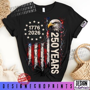 Puede incluir: Camiseta negra con un dise&ntilde;o de la bandera estadounidense, el texto "1776 2026" y "250 YEARS". El dise&ntilde;o incluye una cabeza de &aacute;guila calva y rayos. La camiseta tiene una manga enrollada y un peque&ntilde;o logotipo.